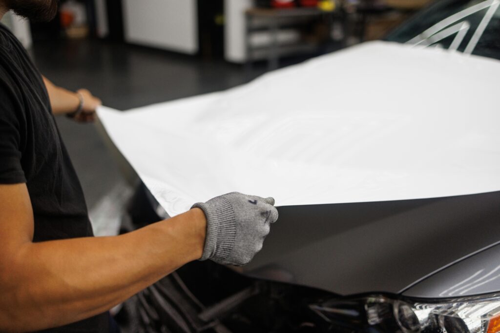 pexels-photo-10126661-10126661 Person applying vinyl wrap to car hood in garage setting.