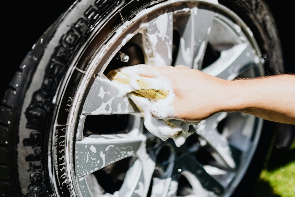 pexels-photo-4870705-4870705 A close-up image of a hand scrubbing a car rim and tire with suds, emphasizing car wash detail.